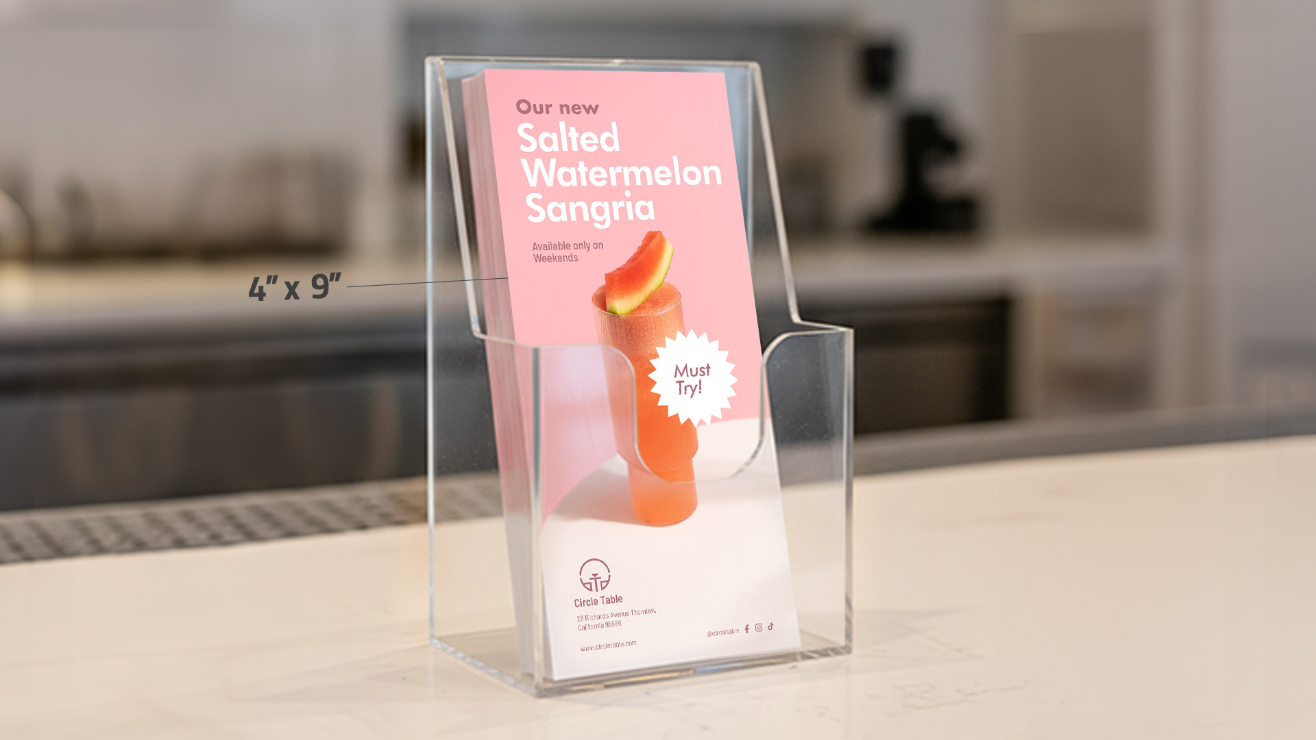 A 4"x9" drink menu rack card displayed in a clear acrylic holder on a counter.